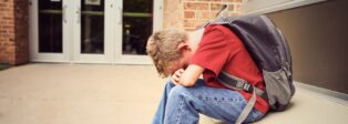Schulangst und Schulverweigerung - Junge sitzt vor Schule, Kopf auf den Knien