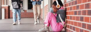 Kind mit Kopfhörern in der Schule, das Gesicht in den Armen vergraben