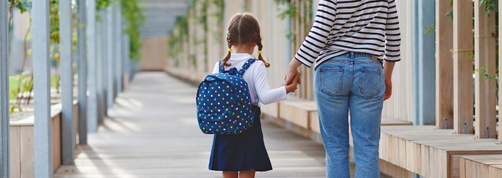 Mädchen hält die Hand der Mutter, Blick zur Schule